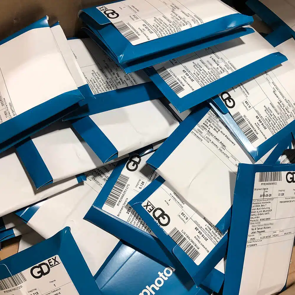zensmart is showing A pile of blue and white GDex shipping envelopes, each containing shipping labels with barcodes and addresses, lies stacked and scattered in a seemingly unorganized manner, reminiscent of a chaotic direct mail marketing campaign. with print workflow automation