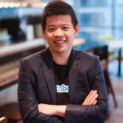 zensmart is showing A man with short black hair, wearing a navy blazer and black shirt, stands indoors with his arms crossed, smiling at the camera. The background is blurred, showing a modern interior with large windows. with print workflow automation